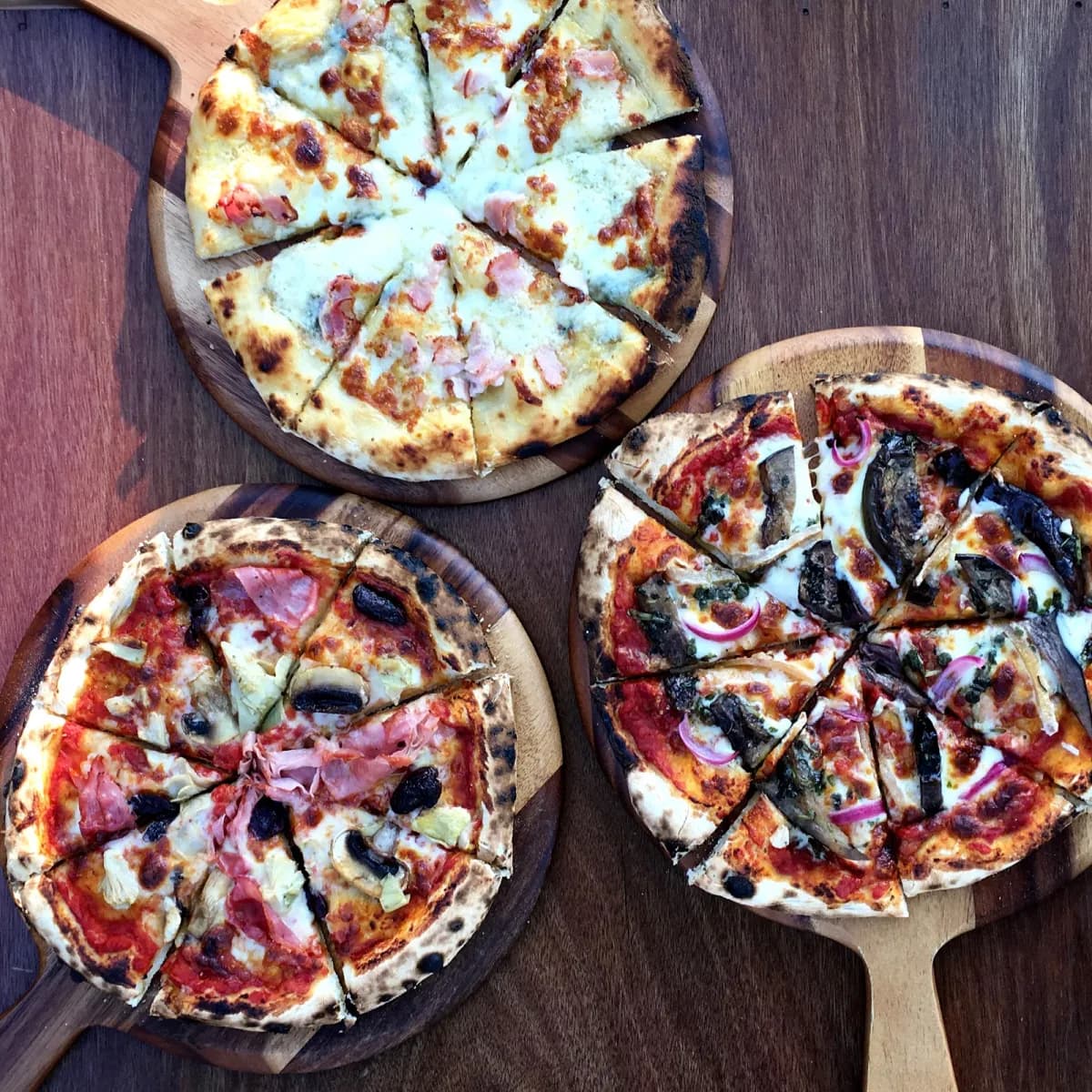 Three woodfired pizzas on rustic boards at Lucky Bat